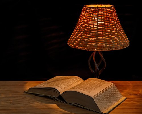 Person reading on a smartphone in bed with a warm bedside lamp on